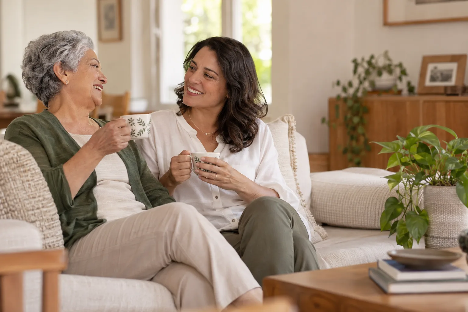 Mulher idosa conversa com uma familiar enquanto tomam chá em casa